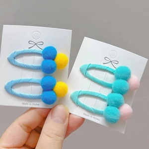 Detail of colorful pom pom hair clips set on hand featuring soft fabric wrapped BB clips