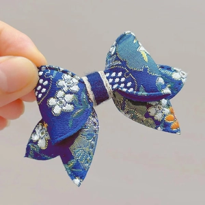 Dettaglio del fiocco blu per capelli con ricamo floreale oro e bianco e texture in raso