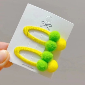 Kids plush pom pom hair clips in neon yellow and green on a white display card