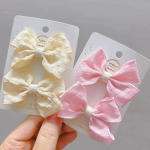 Détail de barrettes à nœuds en tissu crème et rose pour filles sur carte de présentation