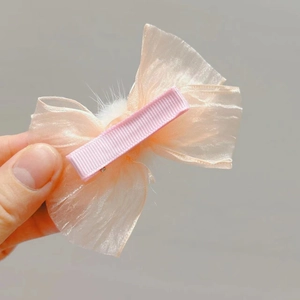 Detalle de pinza para el pelo con lazo de tul rosa, pompón blanco y clip metálico forrado