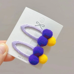 Detailed view of soft purple and yellow pompom hair clips for girls on display card