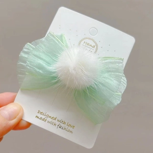 Detalle de pinza para el pelo de tul verde claro con pompón blanco en una tarjeta