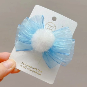 Detalle de una pinza para el cabello con lazo de malla azul y pompón de pelo blanco