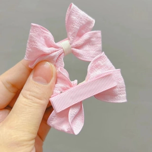 Détail de barrettes à nœuds en tissu rose montrant le ruban texturé et le clip en métal