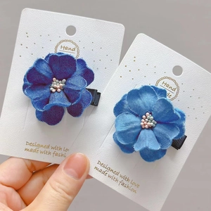 Detail of handmade denim camellia hair clips in navy and light blue on display card