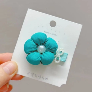 Close-up of a teal fabric flower hair clip with pearl center on a display card