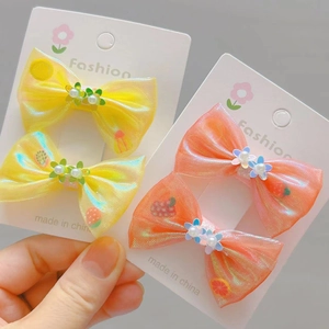 Détail de barrettes à nœuds colorés avec perles et fleurs sur tissu résille à motif fruits