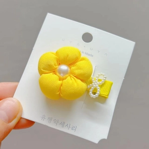 Detail of yellow fabric flower hair clip with large faux pearl and bow on card