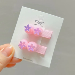 Detail of pink pompom hair clips with purple flower sequins on ribbon-wrapped metal base