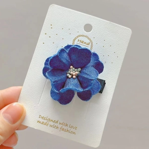 Handcrafted dark blue denim camellia flower hair clip with pearl stamen on display card