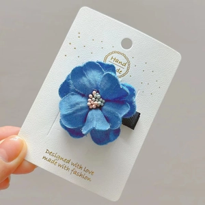 Blue denim camellia flower hair clip with colorful bead center on display card