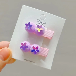 Close-up of children's pink ribbon hair clips with purple pom-poms and sequin petals