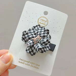 Handmade houndstooth flower hair clip with blue pearl center on grey background