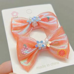 Détail de barrettes nœuds en maille rose avec motifs fruits et fleurs perlées