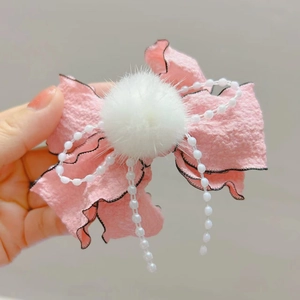 Dettaglio del fermaglio per capelli con fiocco rosa, pompon in pelliccia e finte perle