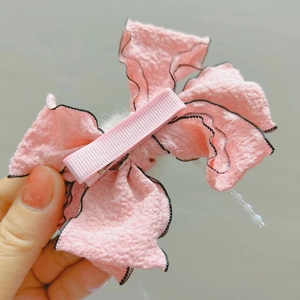 Dettaglio di un fermaglio per capelli a fiocco rosa con bordi neri e perla decorativa