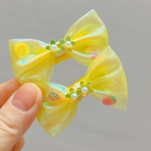 Détail de barrettes à nœud jaune avec tulle irisé, paillettes, perles et motifs de fruits