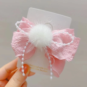 Dettaglio del fermaglio a fiocco rosa con pompon bianco e perle sintetiche pendenti