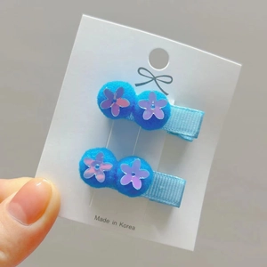 Detailed view of hair clips with blue pompoms and purple sequin flowers on cards