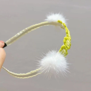 Detail of yellow crochet headband with white faux fur pom poms and daisy embroidery motifs