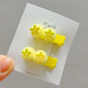 Detail view of yellow sequin flower hair clips with soft pom-poms on a display card