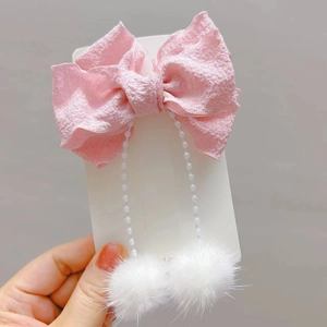 Dettaglio della trama del fiocco in tessuto rosa con perle finte bianche e pompon di pelliccia