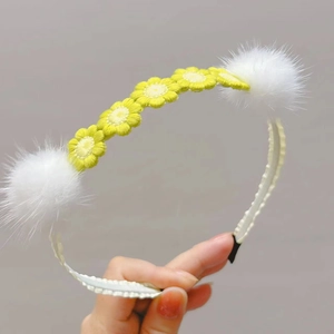 Detail view of five yellow crocheted flowers and white fluffy mink fur balls on headband