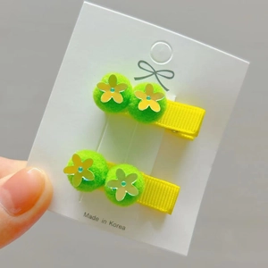 Detail view of yellow ribbon hair clips with green pom-poms and floral sequins for girls