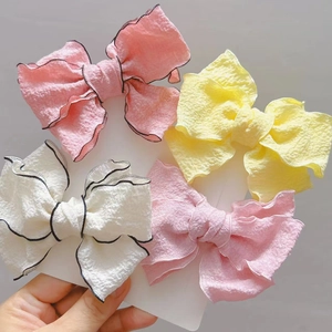 Detail showing textured fabric bow clips in pink, yellow, and white with black trim