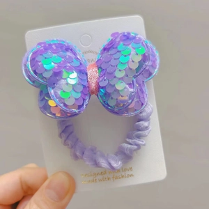 Detailed view of a purple sequin bow hair tie with shimmering fabric on a display card