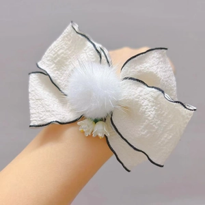 Dettaglio di fiocco bianco per capelli con pompon in peluche e ciondoli di mughetto