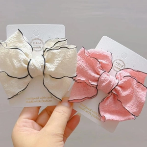 Close-up of beige and pink bow hair clips with bubble fabric and black piped edges