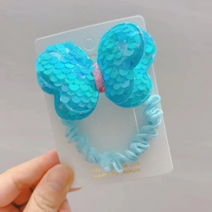 Detailed view of sky blue sequin bow hair scrunchie with glitter center on display card