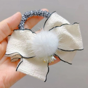 Dettaglio di un fermaglio per capelli a fiocco bianco con pompon e elastico a quadretti