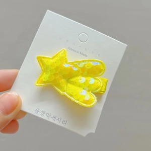 Sparkly yellow sequin star hair clip with meteor tail on a white card display