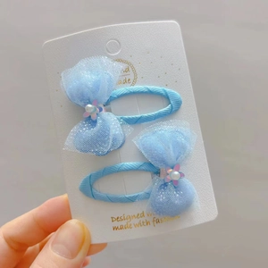 Close-up of light blue mesh bow hair clips with pearls and flowers on card