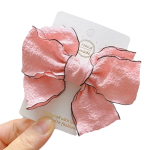 Pink three-layer bow hair clip with textured fabric and black edge on display card