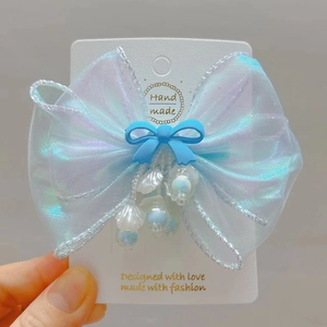 Detail of light blue organza bow hair clip with shell charms and blue bead accents