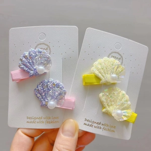 Détail de deux paires de barrettes coquillages avec paillettes arc-en-ciel et perles