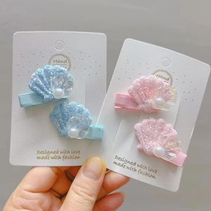 Détail de pinces à cheveux coquillage à paillettes avec perles roses et bleues