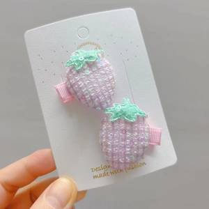 Détail de barrettes fraises avec paillettes roses et feuilles en dentelle sur carte blanche