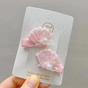 Détail de barrettes coquillage rose avec paillettes et perle sur carte blanche