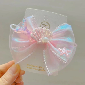 Détail de la barrette à nœud en tulle rose iridescent avec coquillage et queue de sirène