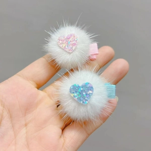 Detail view of plush faux fur hair clips with sparkling heart sequins in pink and blue