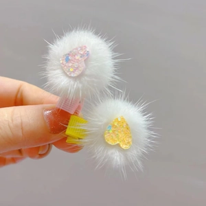 Close-up of white mink fur heart hair clips with glittering pink and yellow centers