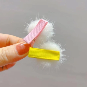 Close-up of plush mink fur ball hair clips in pink and yellow with ribbon wrapped base