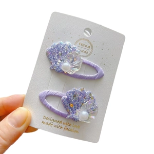 Barrettes coquillage violettes avec perles et paillettes sur support blanc pur