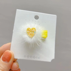 Furry white faux fur hair clip with a sparkling yellow heart on a card display