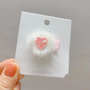 Detail shot of heart-shaped hair clip with white faux fur and pink sequin accents